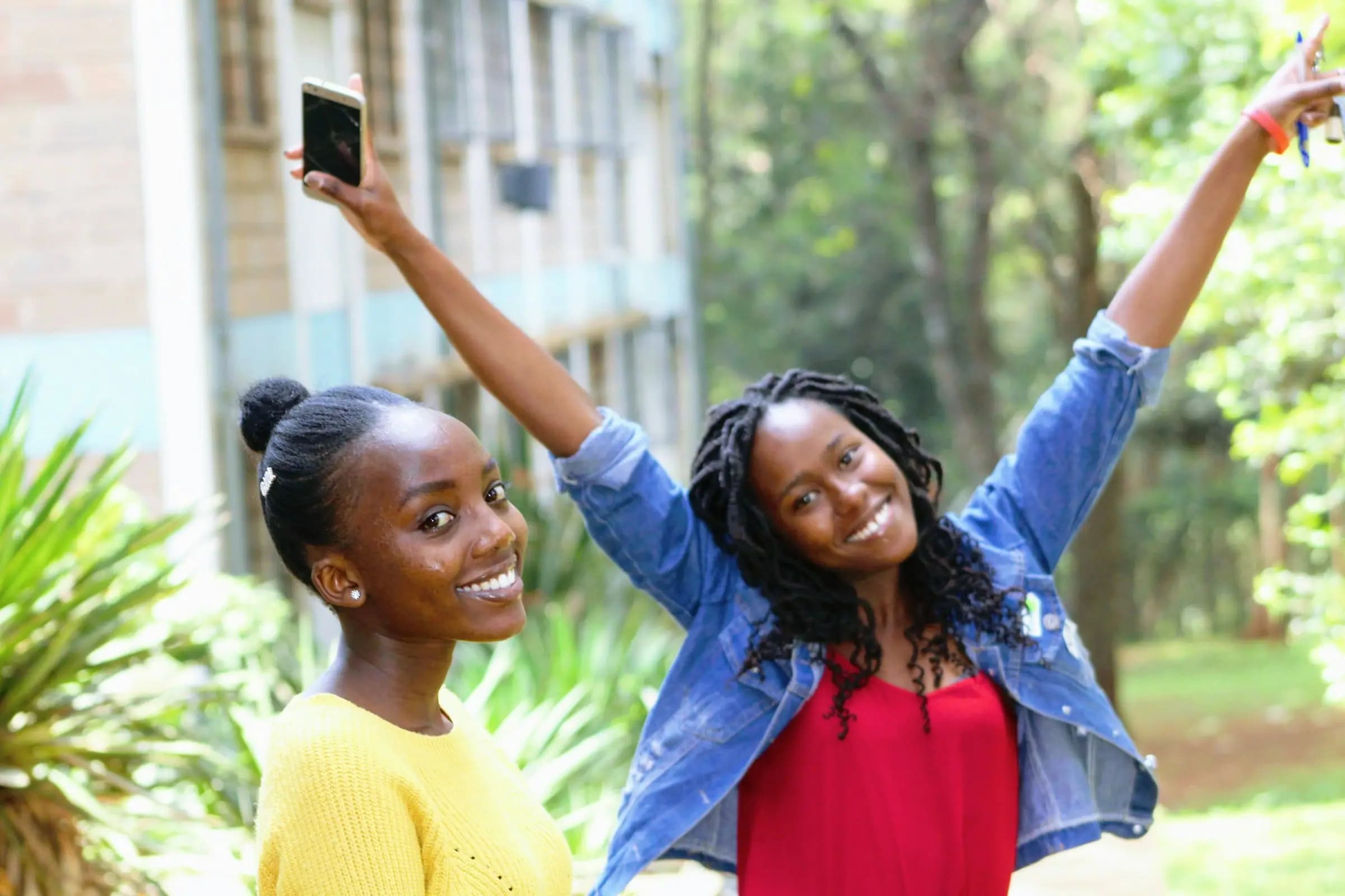 Marafiki wawili wakisherehekea nje, mmoja ameinua simu juu